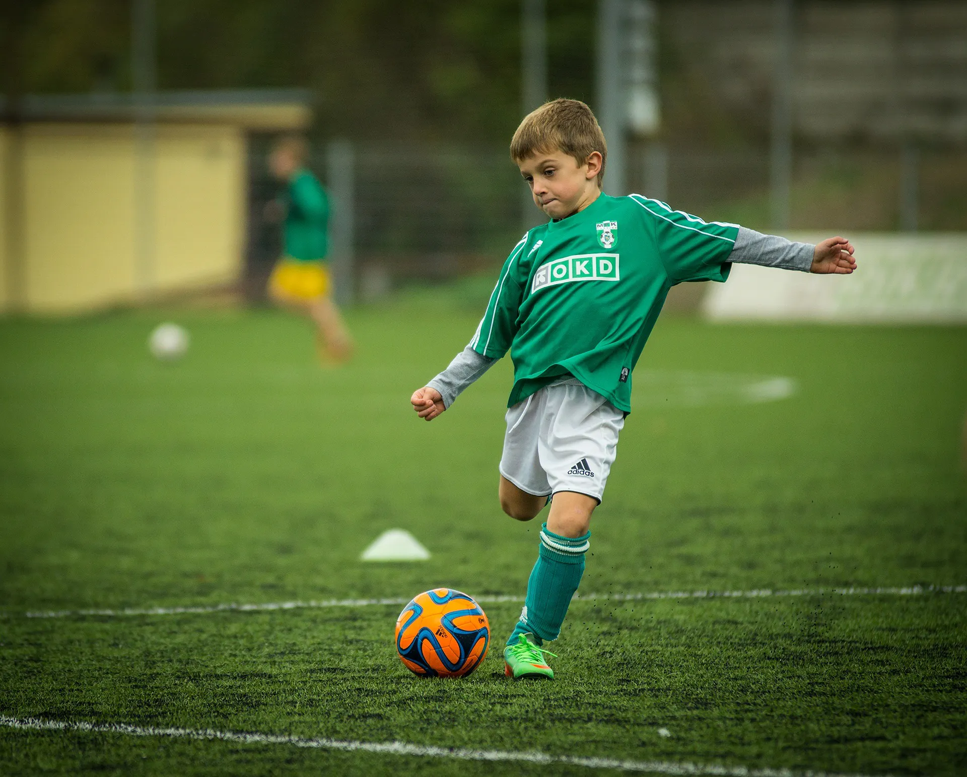 Young boy in a green shirt kicking a soccer ball