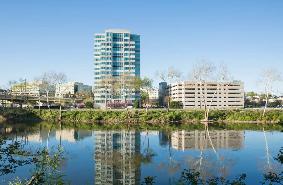 Conshohocken PA office and residential buildings reflected in a calm river under a clear blue sky.