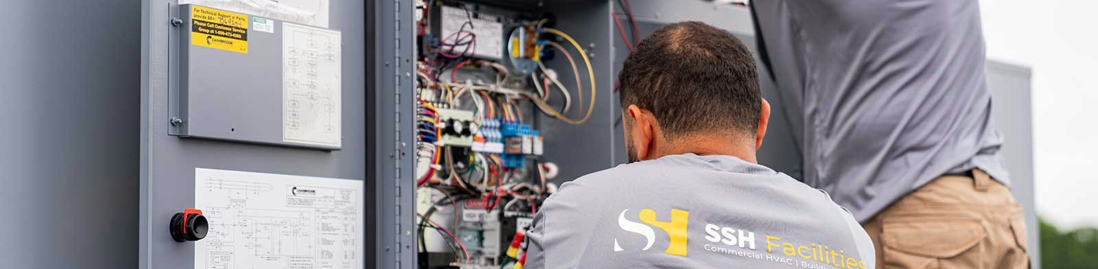 SSH Facilities HVAC technicians troubleshooting electrical wiring and control systems inside commercial rooftop HVAC equipment.