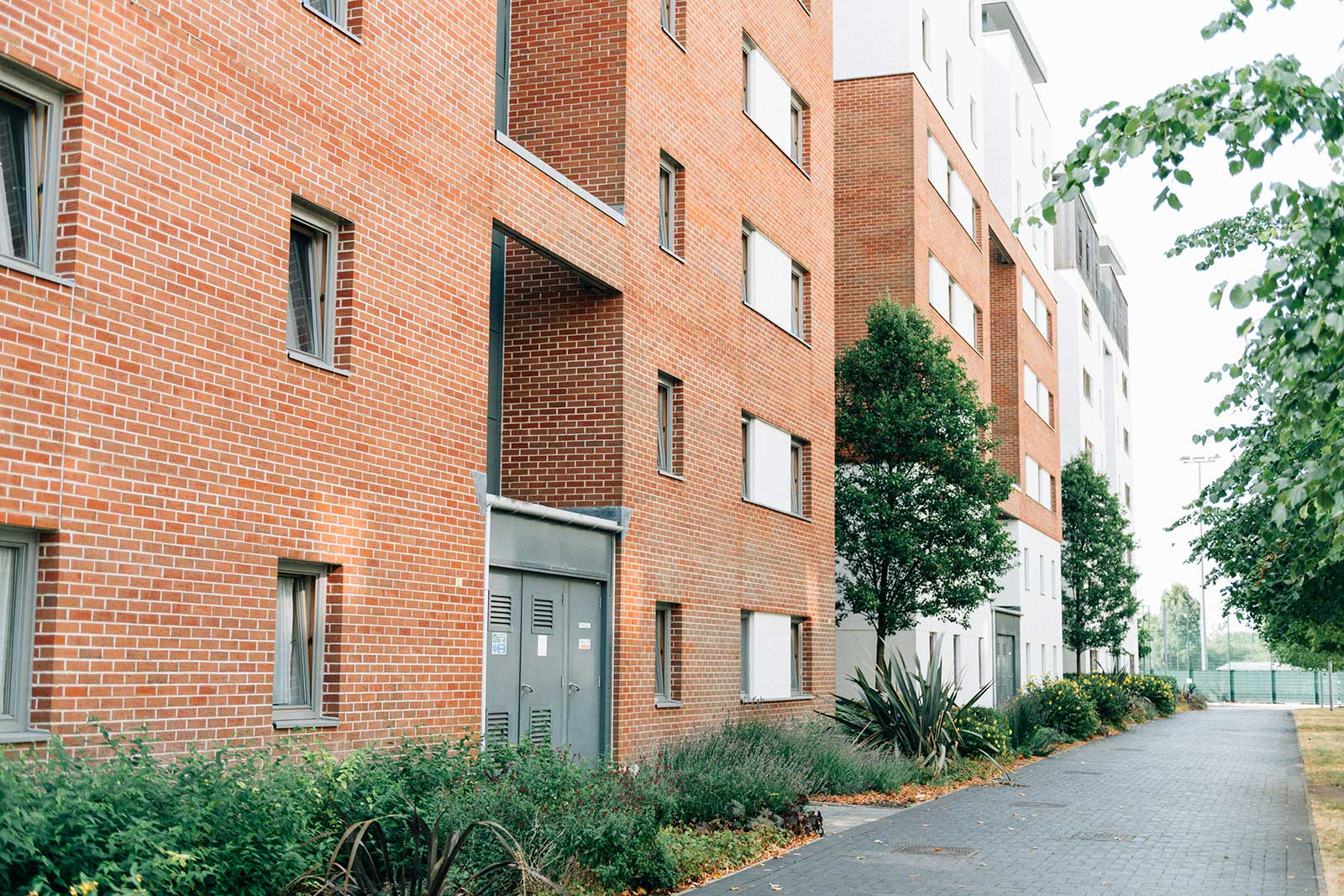 Modern multi-family apartment building with brick exterior, landscaped walkway, and residential entrances.