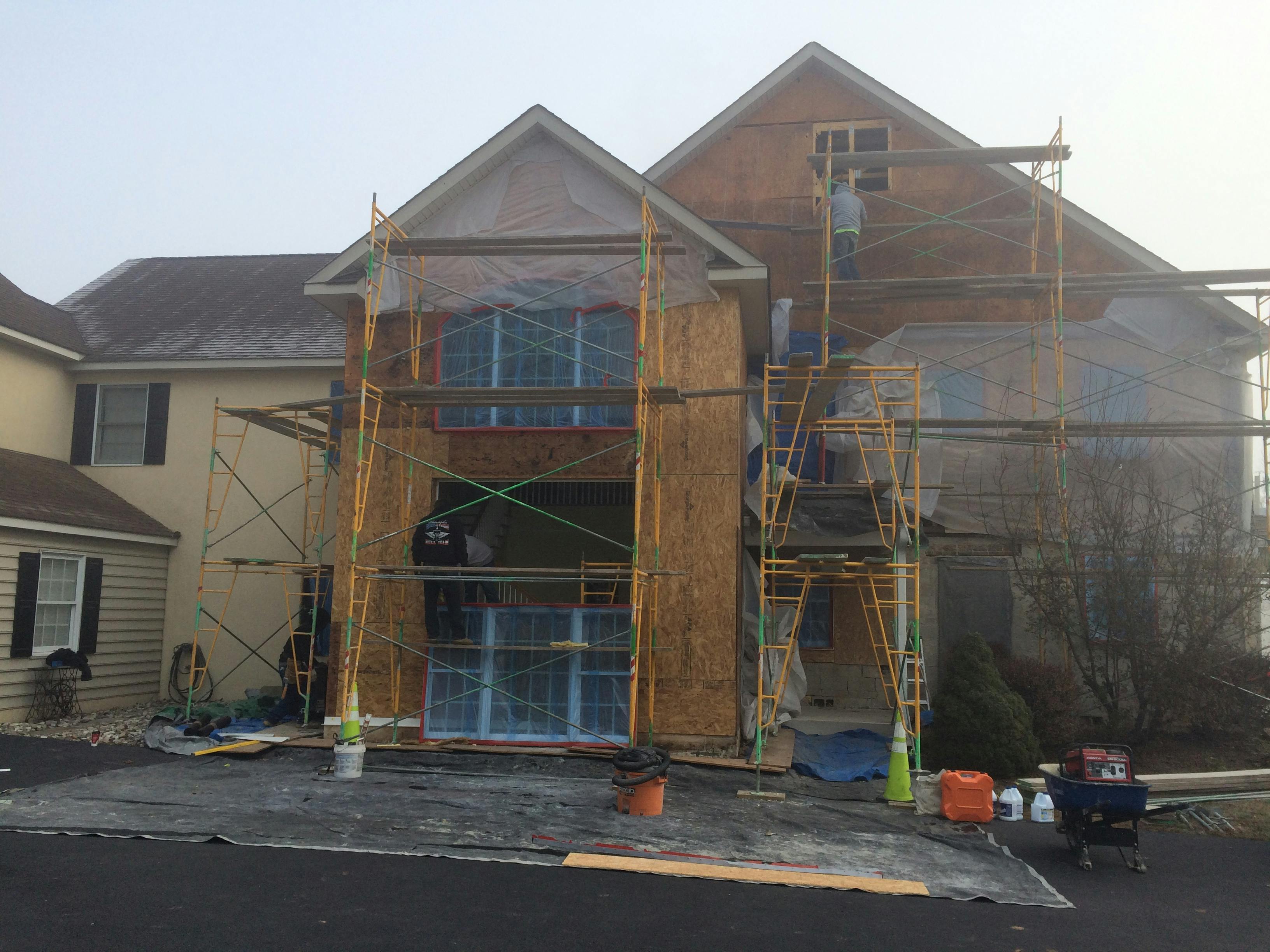 stucco removal process on home with worker on scaffolding